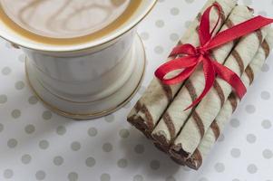 rollo de oblea con cobertura de chocolate y cacao y taza de café con leche foto