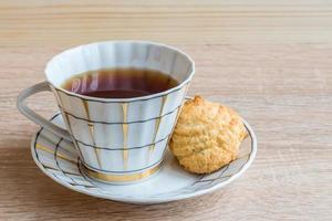 taza de té negro y galleta crujiente aislada en una mesa de madera foto