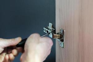 Closeup of worker's hands fitting wardrobe hinge doors in closet photo