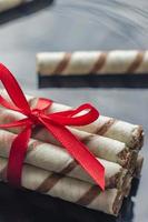 wafer rolls with chocolate and red ribbon on black background photo