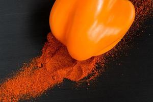 orange bell pepper and paprika powder on black background, top view photo