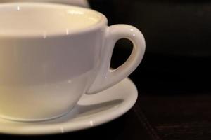 close up of white tea cup and saucer on table. Soft focus photo