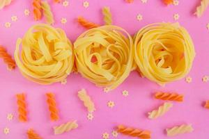 Raw Tagliatelle, fusilli and Stelline pasta scattered on pale pink background. Top view, flat lay photo