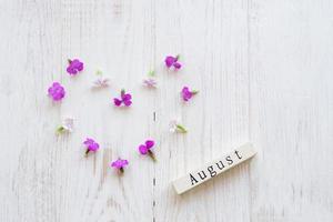 top view of wooden calendar with August sign and pink flowers. photo