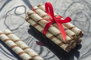 rollos de oblea con chocolate y cinta roja sobre fondo negro foto