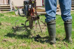 Farmer in rubber boots and blue jeans plows a soil with smal motor tractor. photo