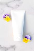 Mockup of white squeeze bottle cosmetic cream tube for branding of medicine or cosmetics - shampoo, gel, skincare. Moisturizer blank bottle and pansy flowers on marble background. Top view. photo