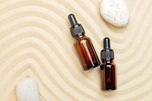 Dark Glass bottles of moisturizing face serum, cosmetic oil and pebble stones on a sandy background. Summer facial skin care concept. photo