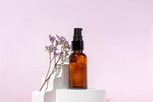 Pump amber glass cosmetic bottle with cream or fluid for skin care on white concrete podium on pink background. Natural skin care concept. photo