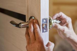 hombre reparando el pomo de la puerta. primer plano de las manos del trabajador instalando un nuevo casillero en la puerta foto