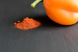 orange bell pepper and paprika powder on black background, copy space for your text photo