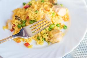 paella with chicken and seafood on white plate. Spanish dish served on table. Shrimp on a fork photo