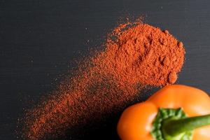 orange bell pepper and paprika powder on black background, top view photo