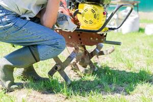 man in rubber boots starts a tractor motoblock for plowing fields photo