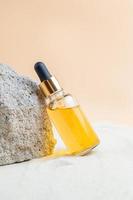 Dropper bottle of moisturizer, serum or Vitamin C oil for face on stones with sand, sand background, summer face care photo