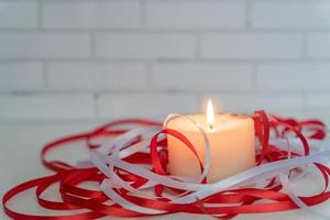 White burning candle with white and red ribbons on table photo