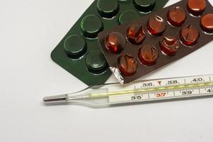 píldoras de medicina y termómetro sobre fondo blanco foto