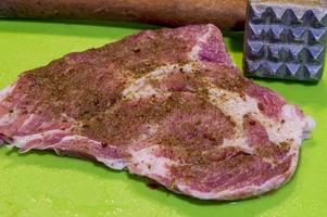 filete de cerdo crudo con especias y ablandador de carne sobre fondo verde foto