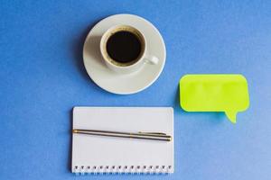 taza de café negro con cuaderno, pegatina y bolígrafo sobre fondo azul claro. concepto de negocio tonificado con espacio de copia foto