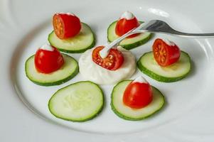 Cherry tomatoes an sliced cucumbers with mayoneese sauce on a plate. Fresh salad photo