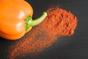 orange bell pepper and paprika powder on black background, top view photo