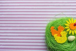 nido artificial verde con dos gallos de colores, huevo y girasol sobre fondo rayado foto