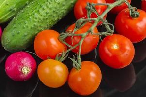 red toatoes and green cucumbers on black background photo