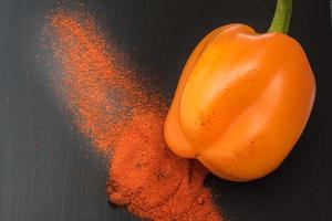 orange bell pepper and paprika powder on black background, top view photo