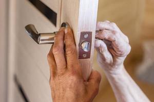 man repairing the doorknob. closeup of worker's hands installing new door locker photo