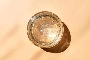 Jar with transparent cosmetic product, gel or cream on beige colored background. Unbranded package with of antioxidant cream for self-care. View from above. photo