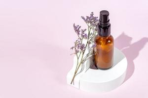 Amber glass bottle with pomp lid on the white podiums. Pink background. Container mockup with face cream or serum. Showcase for the presentation skincare products. photo