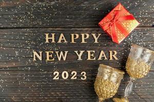 New year presents and champagne glasses on wooden table. Text Happy new year 2023. Festive greeting card. Flat lay. photo