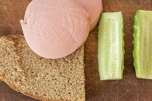 rye bread, cucumber and sausage on brown wooden desk photo