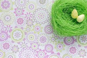 Artificial green nest with two eggs on flower background photo