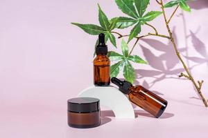 Cannabis face cream and serum or oil dropper concept. Natural cosmetic. CBD oil, THC tincture and hemp leaves on a pink background photo