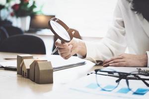 Inspector Concept, a customer is holding a magnifying glass to look at each house model to check the price of a home loan for each model. photo