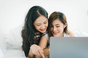 lgbtq, concepto lgbt, homosexualidad, retrato de dos mujeres asiáticas posando felices juntas y amándose mientras juegan a la computadora portátil en la cama foto