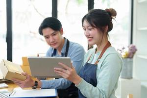 Portrait of a small start-up and SME owner, an Asian male and female entrepreneur checking orders and packing for customers, self-employed, freelance, online selling photo