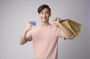 Young asian man holding credit card and shopping bag over white background studio, shopping and finance concept. photo