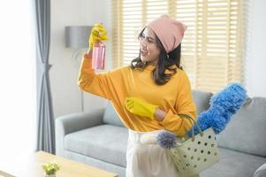 Young happy woman wearing yellow gloves  and holding a basket of cleaning supplies in living room. photo