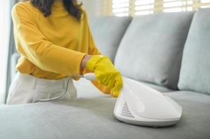 Young happy woman wearing yellow gloves  and vacuum Cleaning a sofa in living room. photo