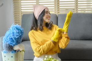 Young happy woman wearing yellow gloves  and holding a basket of cleaning supplies in living room. photo