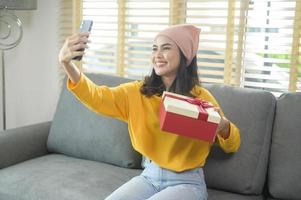 joven mujer sorprendida abriendo una caja de regalo en la sala de estar. foto