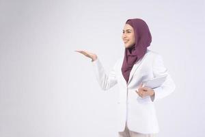 Beautiful muslim business woman wearing white suit with hijab holding tablet in studio photo