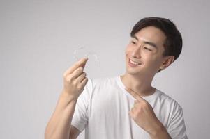 Young smiling man holding invisalign braces over white background studio, dental healthcare and Orthodontic concept. photo