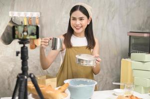 hermosa mujer está haciendo panadería mientras transmite en vivo o graba videos en las redes sociales en su casa, concepto de negocio de cafetería. foto