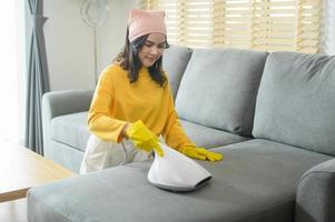 Young happy woman wearing yellow gloves  and vacuum Cleaning a sofa in living room. photo