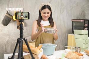 Beautiful woman is making bakery while live streaming or recording video on social media in her house, coffee shop business concept. photo