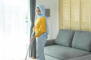 Young happy muslim woman mopping and vacuum the floor in living room. photo