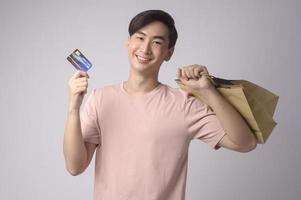 Young asian man holding credit card and shopping bag over white background studio, shopping and finance concept. photo